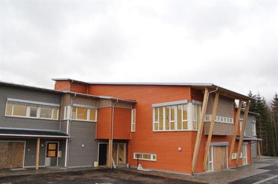 Bilde av Gvarv barnehage. Tofarga bygg i to etasjar i grått og oransje med nesten flatt tak. Asfalt på utsiden.  - Klikk for stort bilde