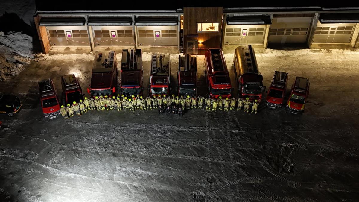 Bilde fra fugleperspektiv. Kvelden. 10 brannbiler med mange brannmannskap i front av bilene. - Klikk for stort bilde